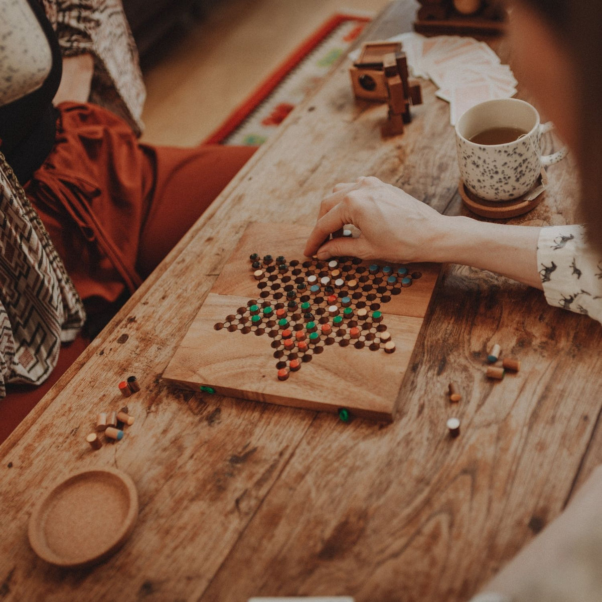 Zwei Personen spielen an einem Tisch ein Holzspiel mit bunten Steinen